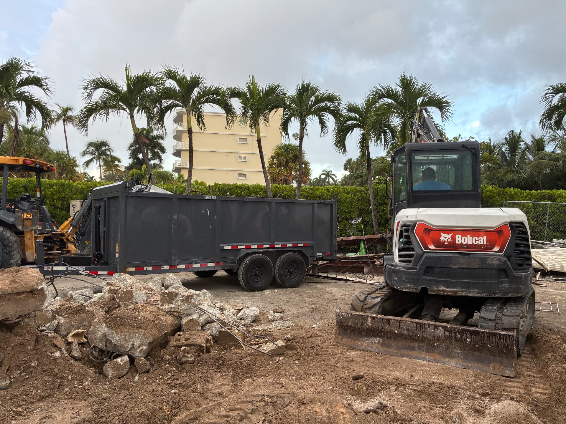 All Out Rubbish Bobcat excavator and John Deere loader staged near piles of broken concrete rubble at a land development site in Palm Beach County, Florida
