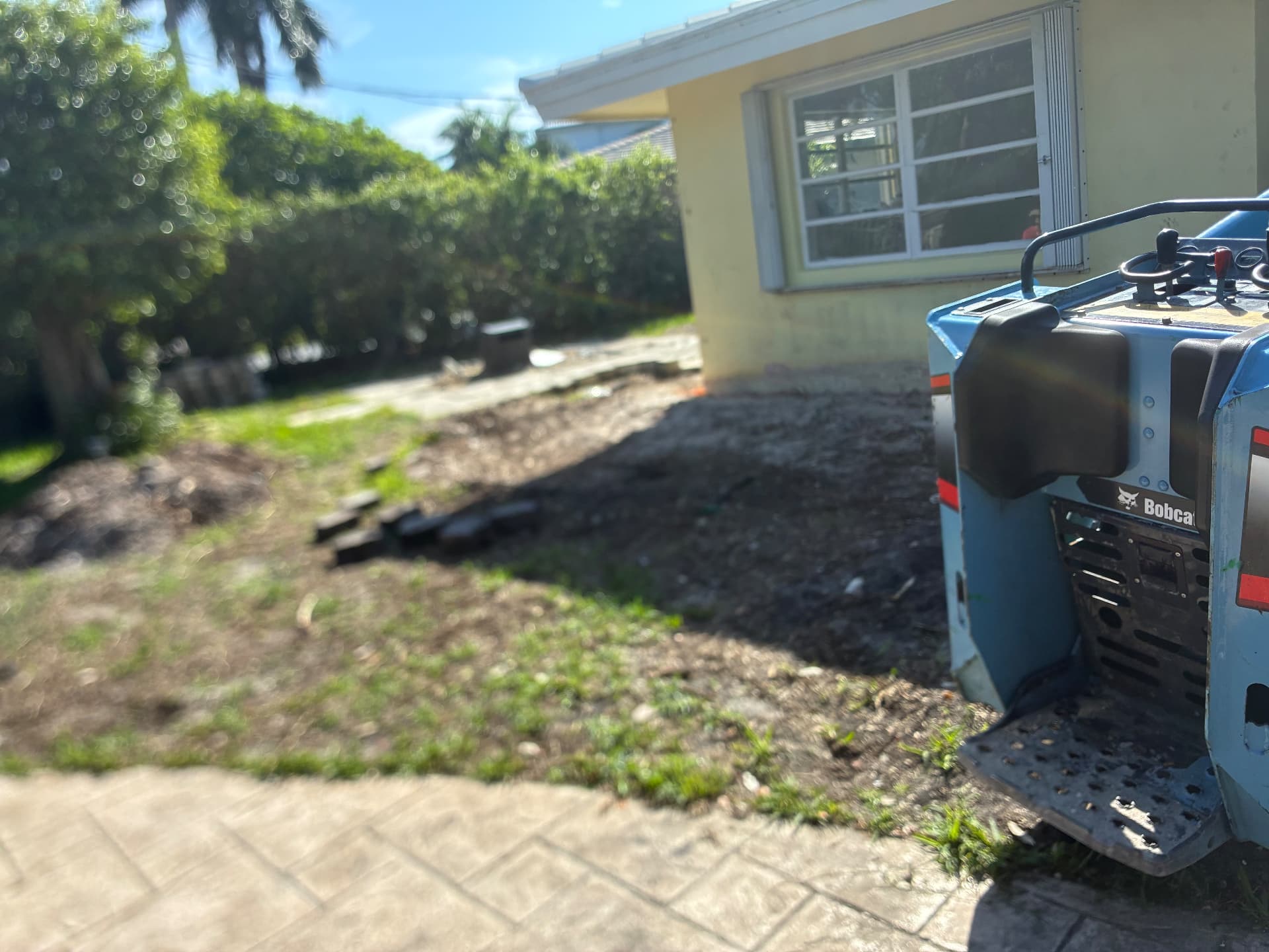 Side yard — Bobcat working the grade — land grading and concrete slab prep by All Out Rubbish in Palm Beach County, Florida