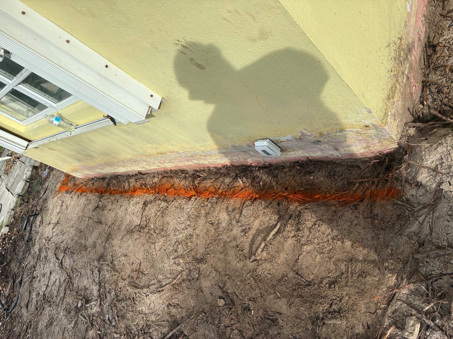Orange cut line along the foundation — root removal — land grading and concrete slab prep by All Out Rubbish in Palm Beach County, Florida