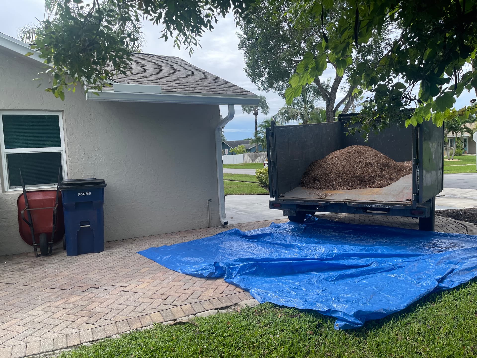 All Out Rubbish dump trailer loaded with soil backed onto a paver driveway with a blue tarp laid out in Palm Beach County, Florida