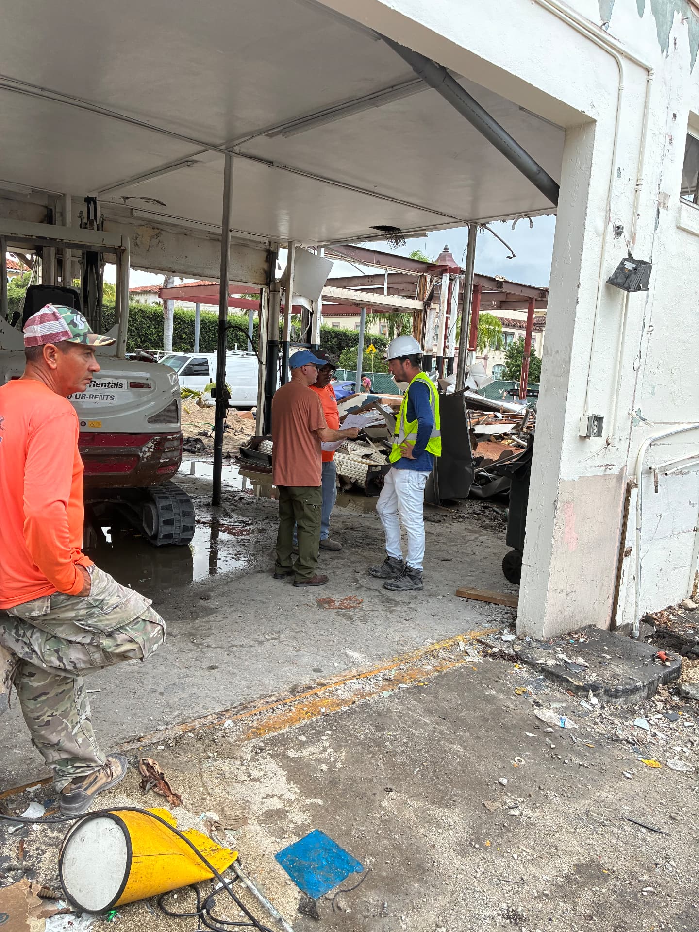 All Out Rubbish crew reviewing plans inside a partially demolished building with a Bobcat compact excavator on site in Palm Beach County, Florida