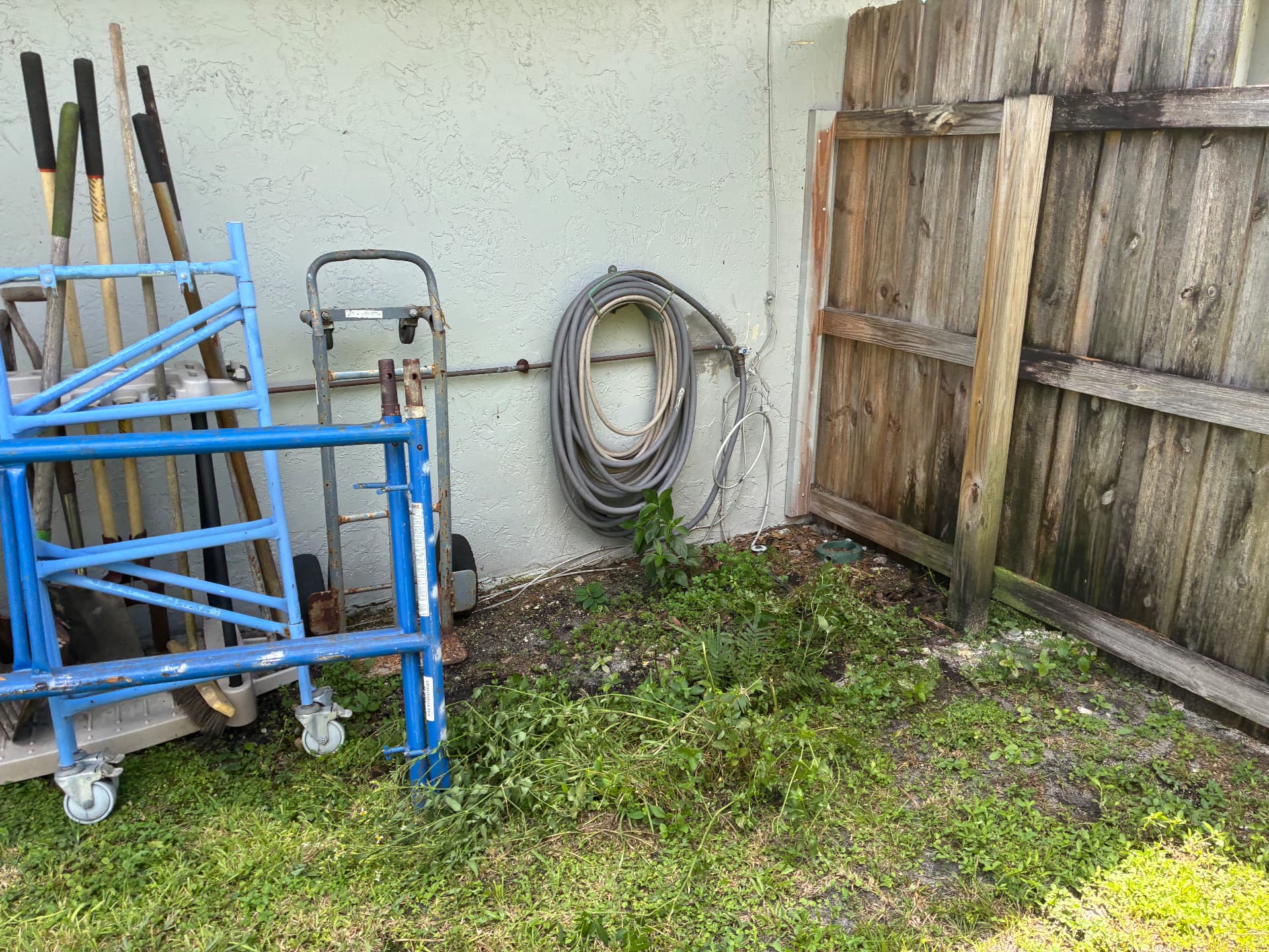 Before junk removal: metal scaffolding, cut green waste and long-handled tools piled against a house wall before cleanup by All Out Rubbish