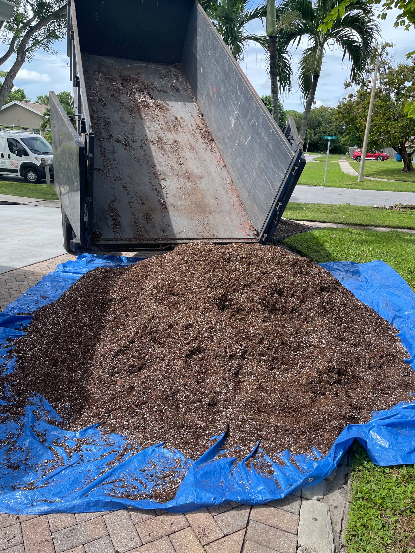 Pile of soil delivered from an All Out Rubbish dump trailer onto a blue tarp on a paver driveway in Palm Beach County, Florida