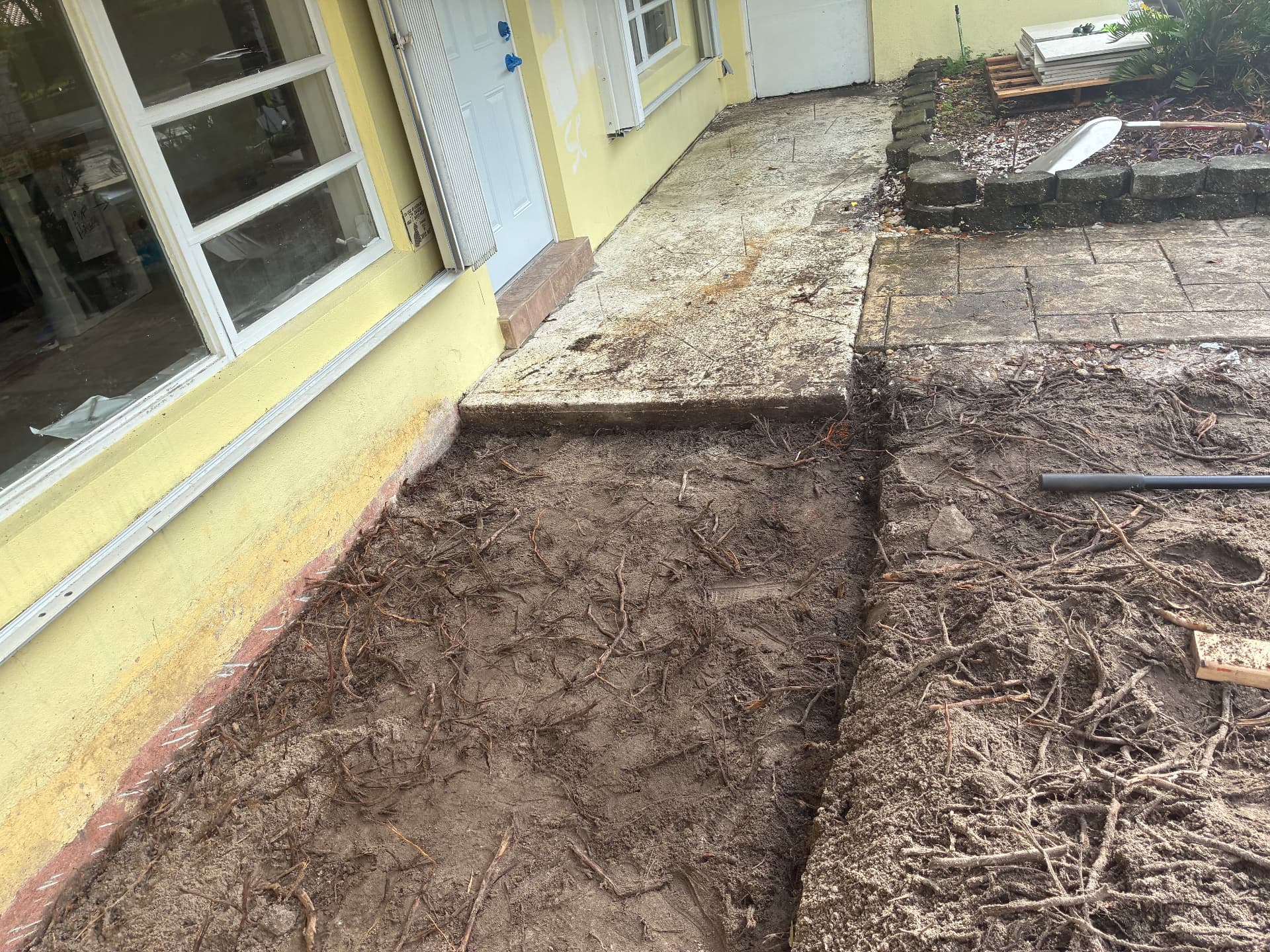 Excavated area along the house — soil and roots cleared — land grading and concrete slab prep by All Out Rubbish in Palm Beach County, Florida