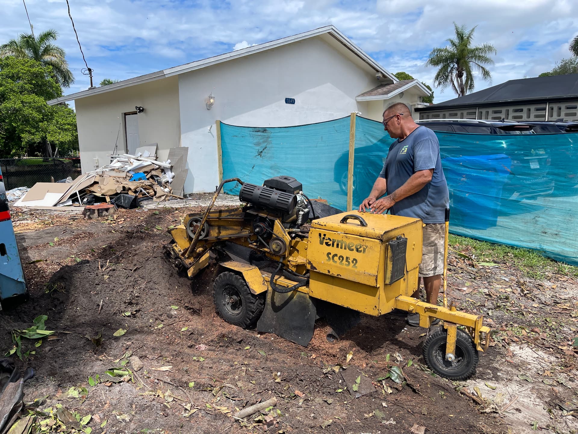 All Out Rubbish crew member running a Vermeer stump grinder on a cleared residential lot in South Florida