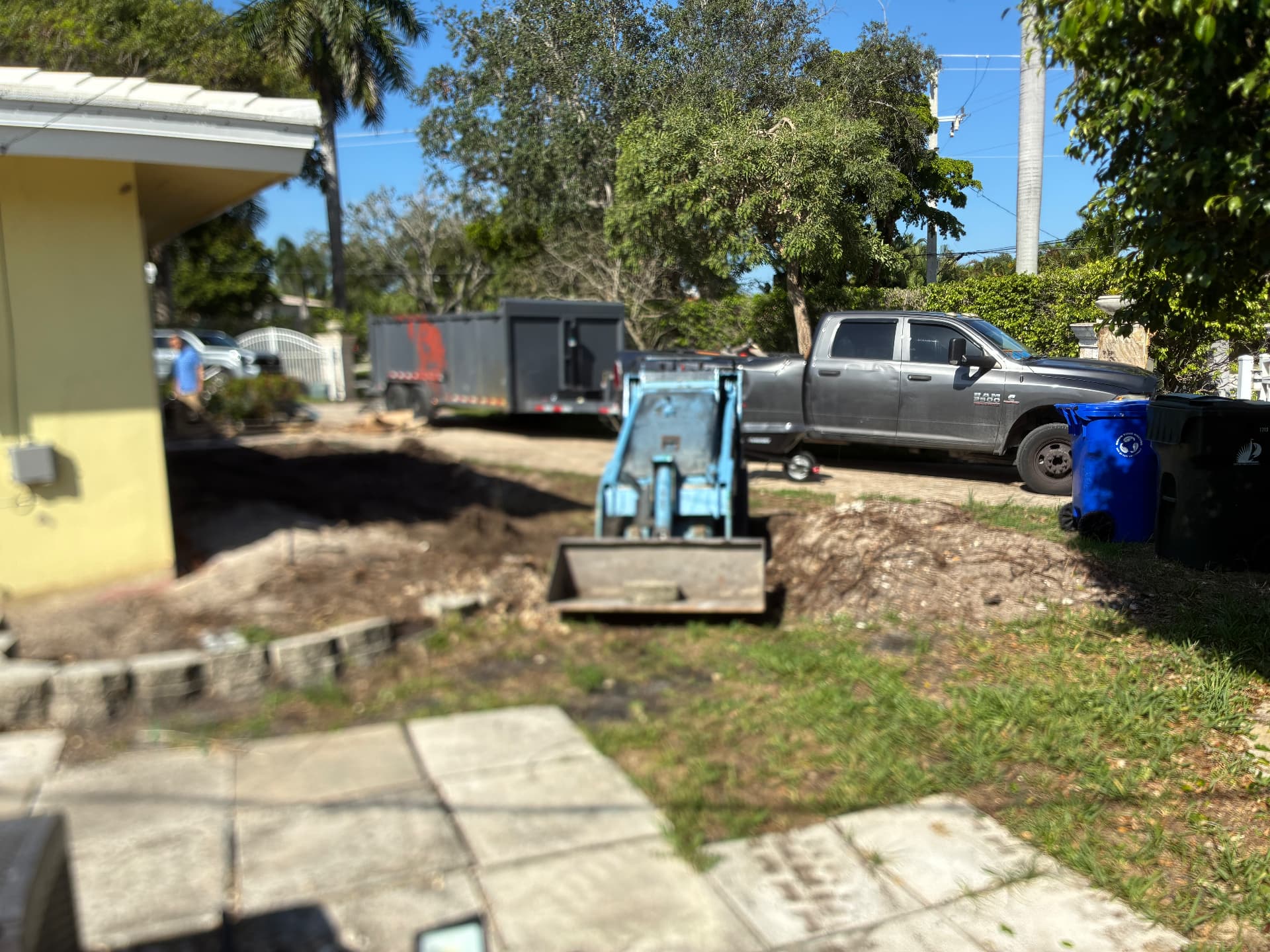 Bobcat MT100 grading the yard — dump trailer staged — land grading and concrete slab prep by All Out Rubbish in Palm Beach County, Florida